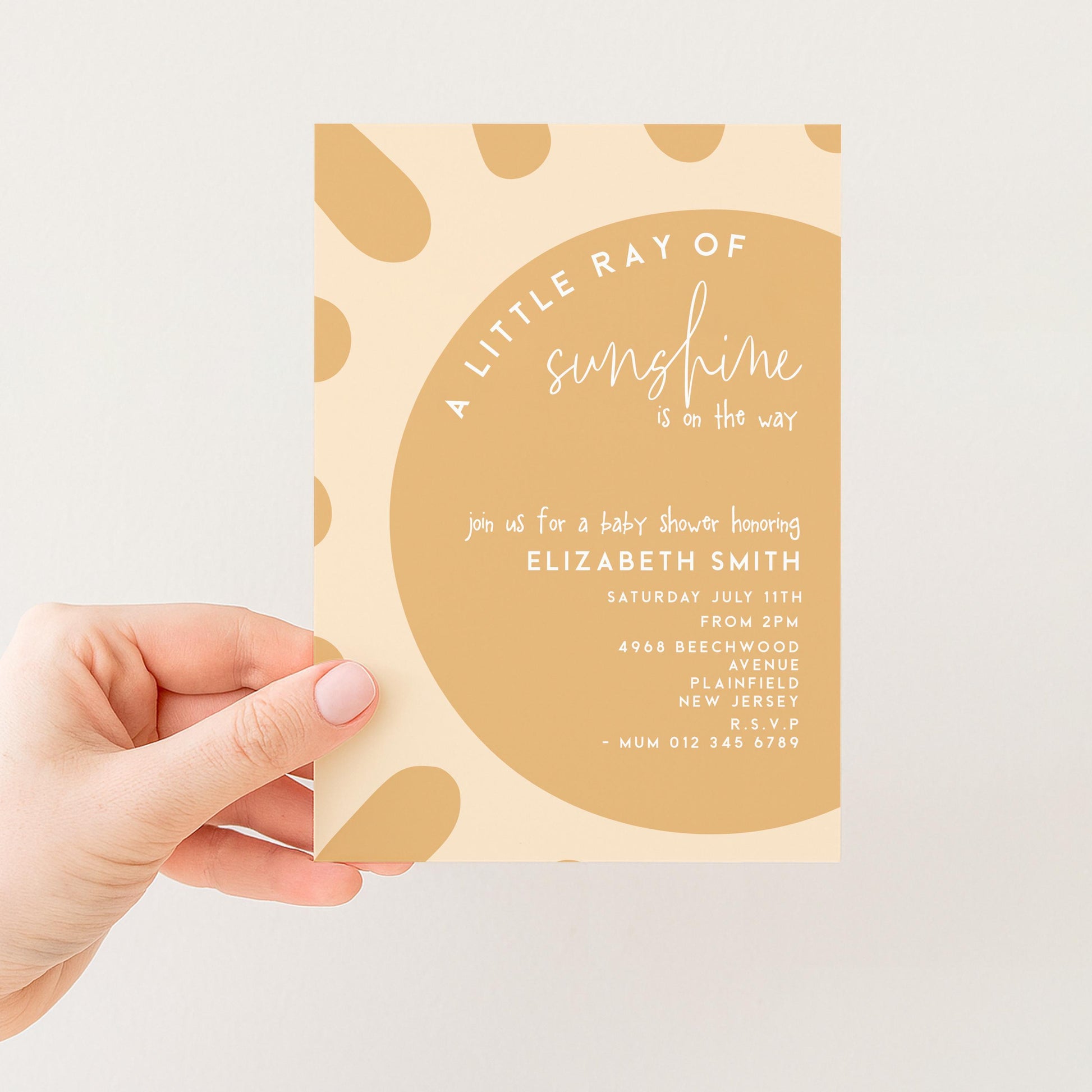 A hand holding a baby shower invitation with a light brown background and a large circle design.