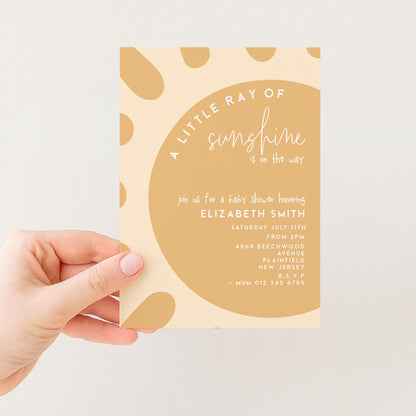 A hand holding a baby shower invitation with a light brown background and a large circle design.