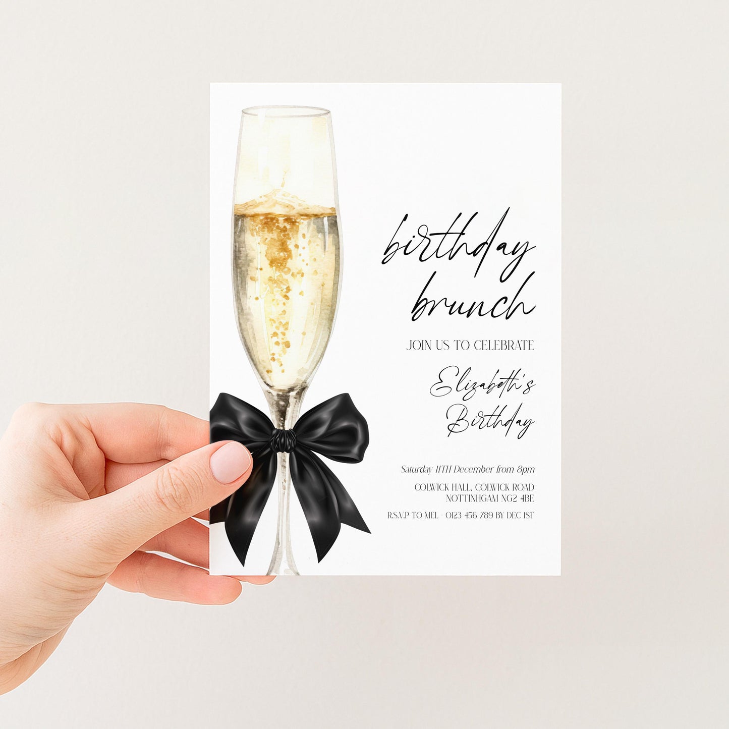 A hand holding a birthday invitation card with a champagne glass and a black bow.