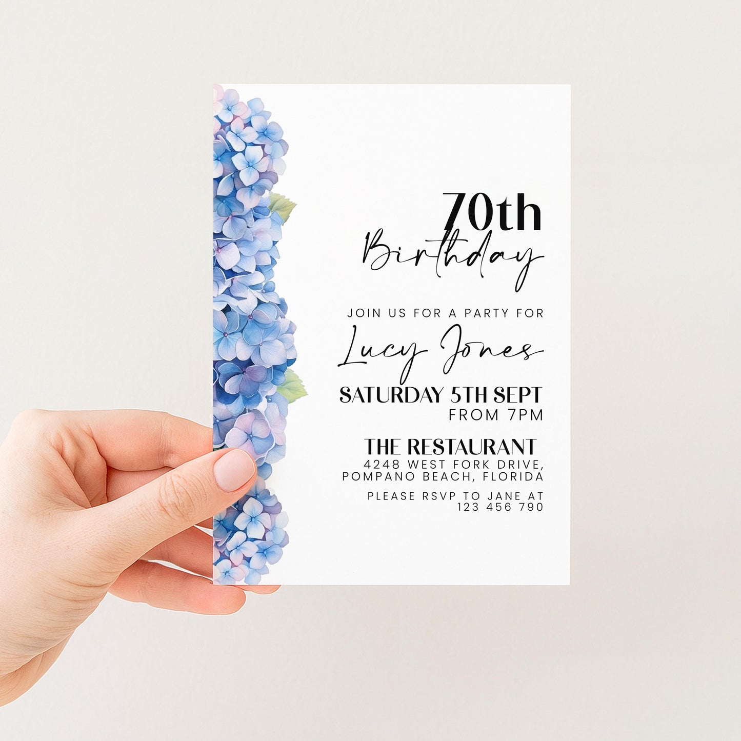 a hand holding a birthday invitation card with a floral design on the left side.