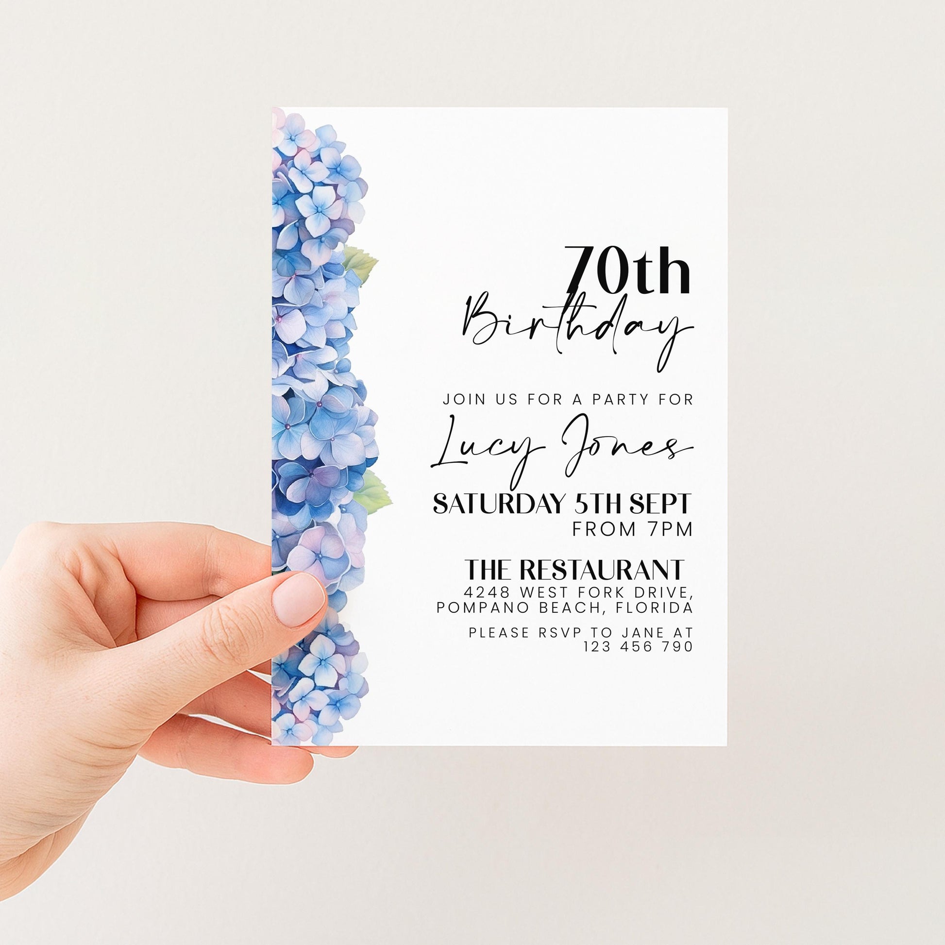 a hand holding a birthday invitation card with a floral design on the left side.