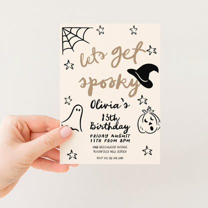 A hand holding a Halloween-themed birthday party invitation card.