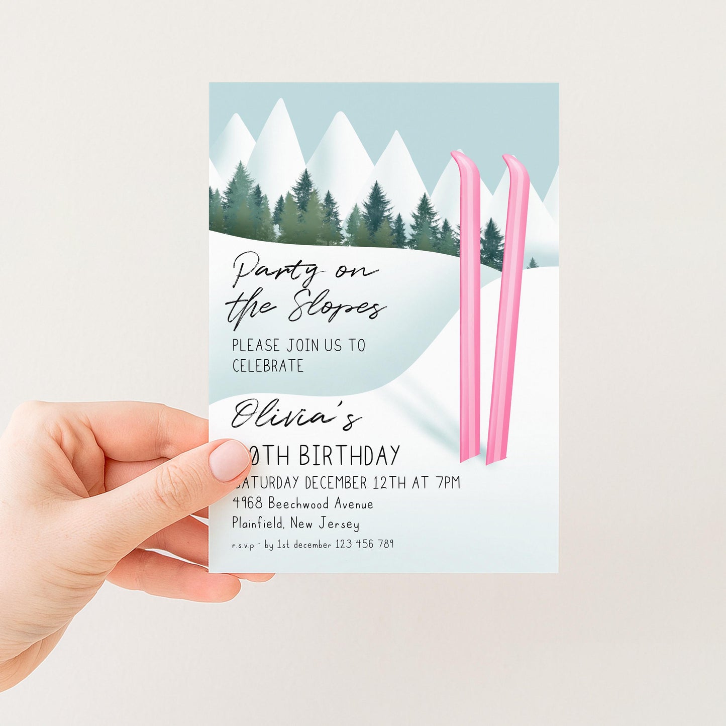 A hand holding a birthday party invitation card with a winter landscape and pink skis.