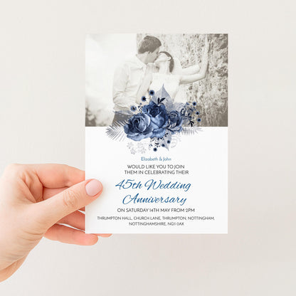 A hand holding a wedding invitation card with a black and white photograph of a couple embracing and a blue floral design.