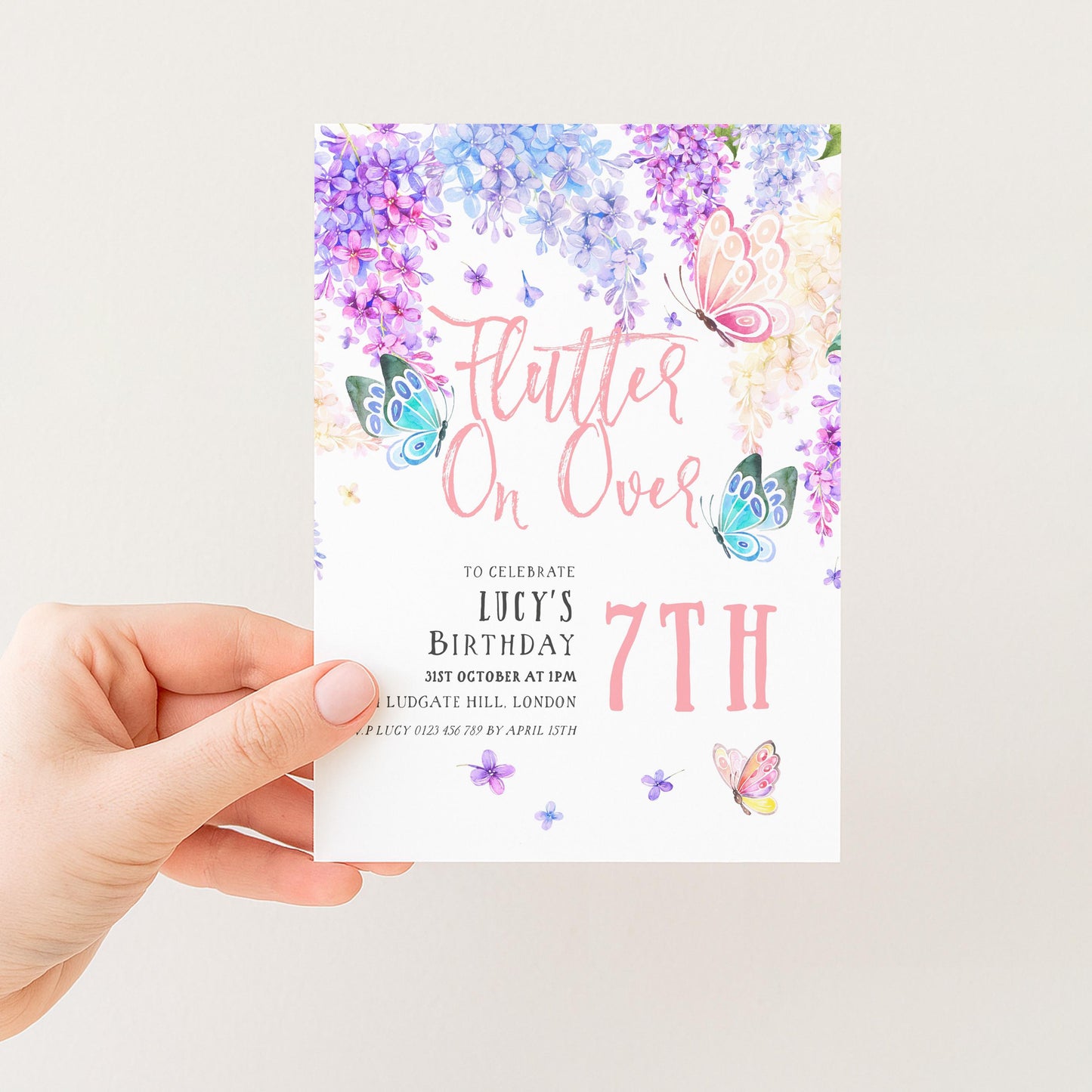A hand holding a birthday invitation card with a floral design and butterflies.