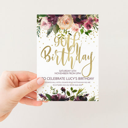 A hand holding a white card with a floral design and gold text.