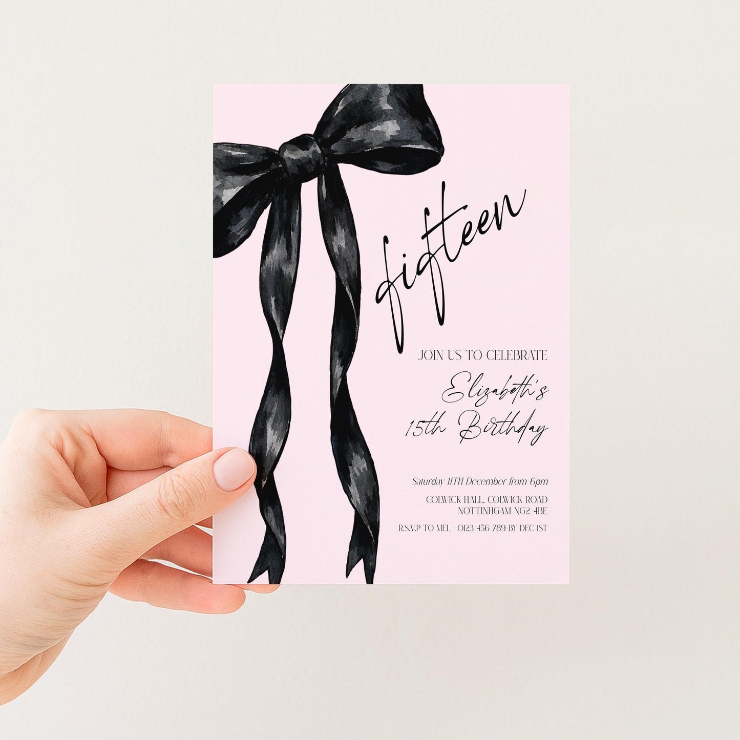 a hand holding a pink invitation card with a black ribbon design.