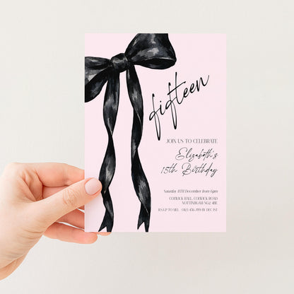 a hand holding a pink invitation card with a black ribbon design.