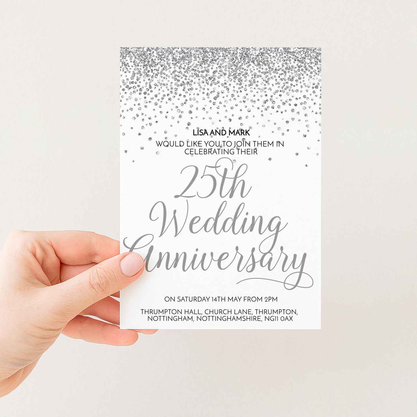A hand holding a wedding anniversary invitation card with a silver glitter design and text.