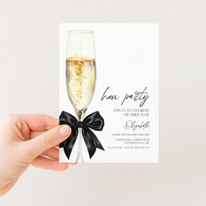 a hand holding a white invitation card with a champagne glass and a black bow on it.