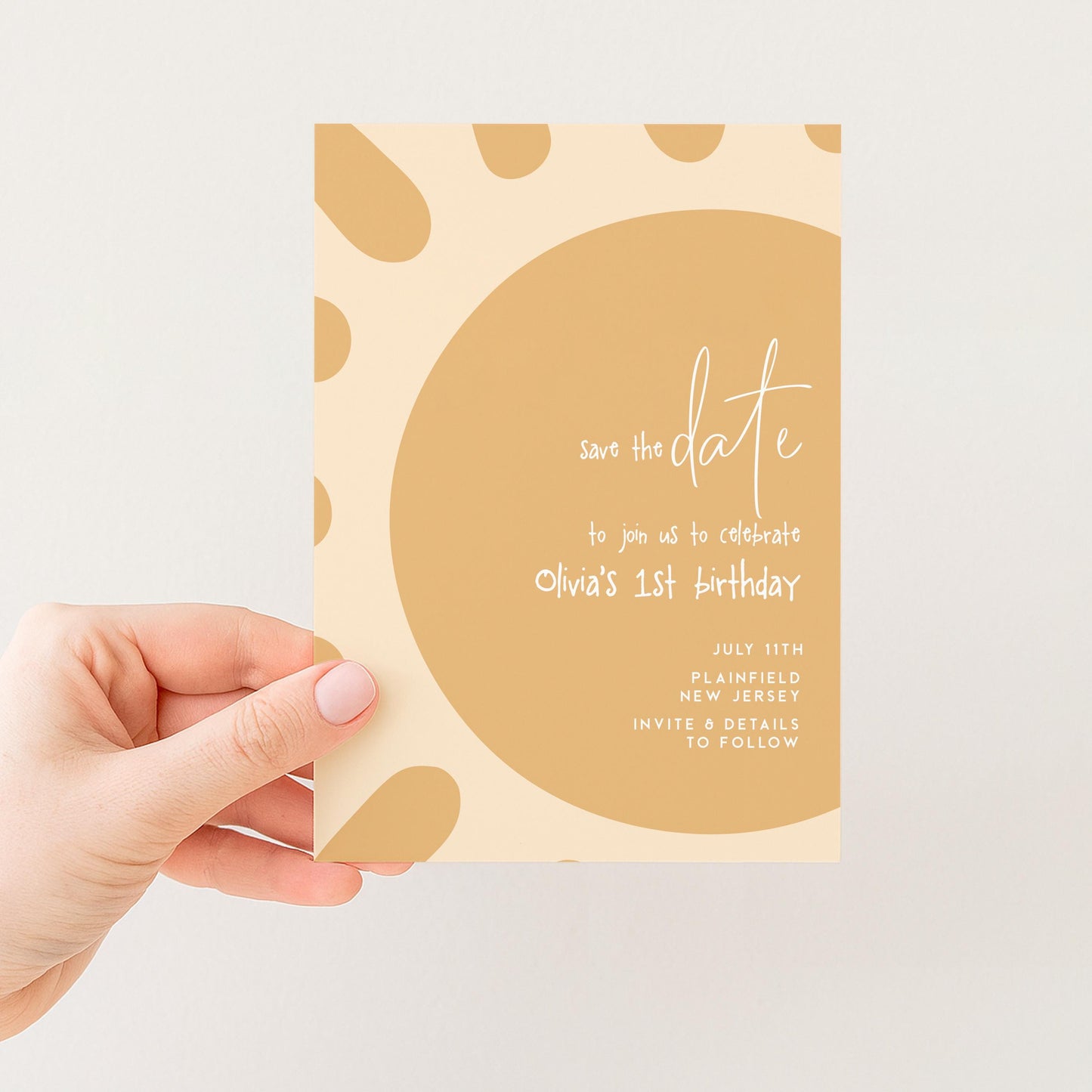 a hand holding a card with a yellow and brown color scheme, featuring a circular design with a sun-like pattern. The card appears to be a save the date card for an event, likely a birthday celebration.
