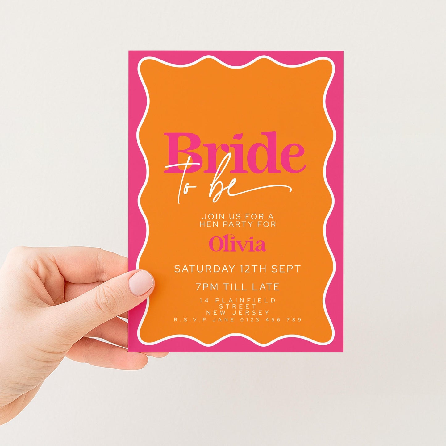 A hand holding a bright orange and pink invitation card with text and details about a bridal party.