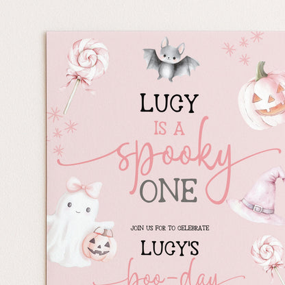 The image is a Halloween-themed invitation card with illustrations of a ghost, a witch's hat, a bat, a pumpkin, and a lollipop. The text on the card reads "LUCY is a spooky one" and invites guests to "JOIN US FOR TO CELEBRATE LUCY'S HOO-DAY".