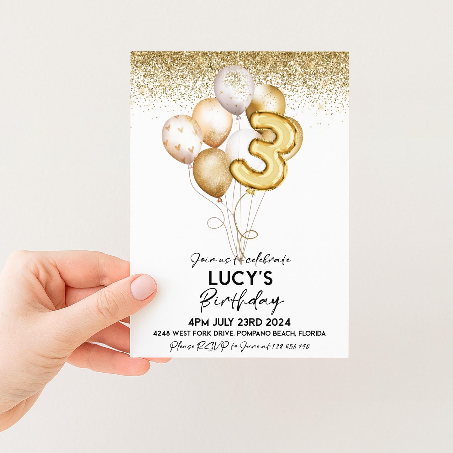 a person holding a birthday invitation card with a gold glitter design and balloons.