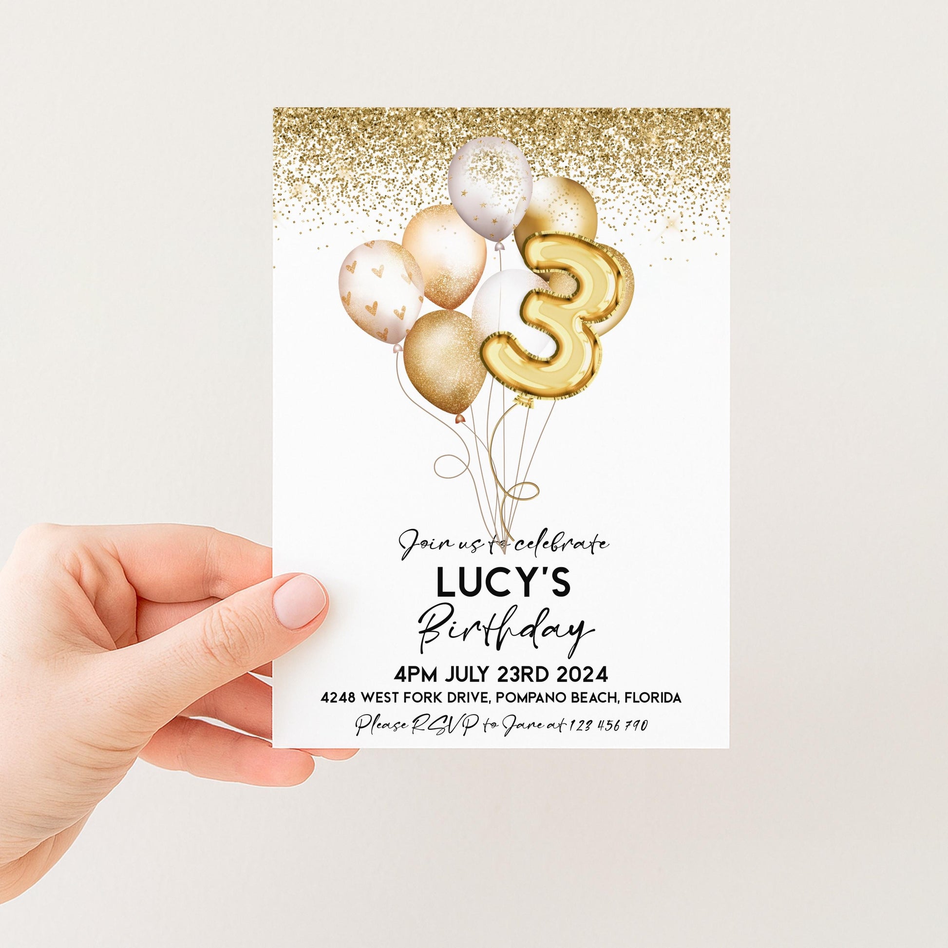 a person holding a birthday invitation card with a gold glitter design and balloons.