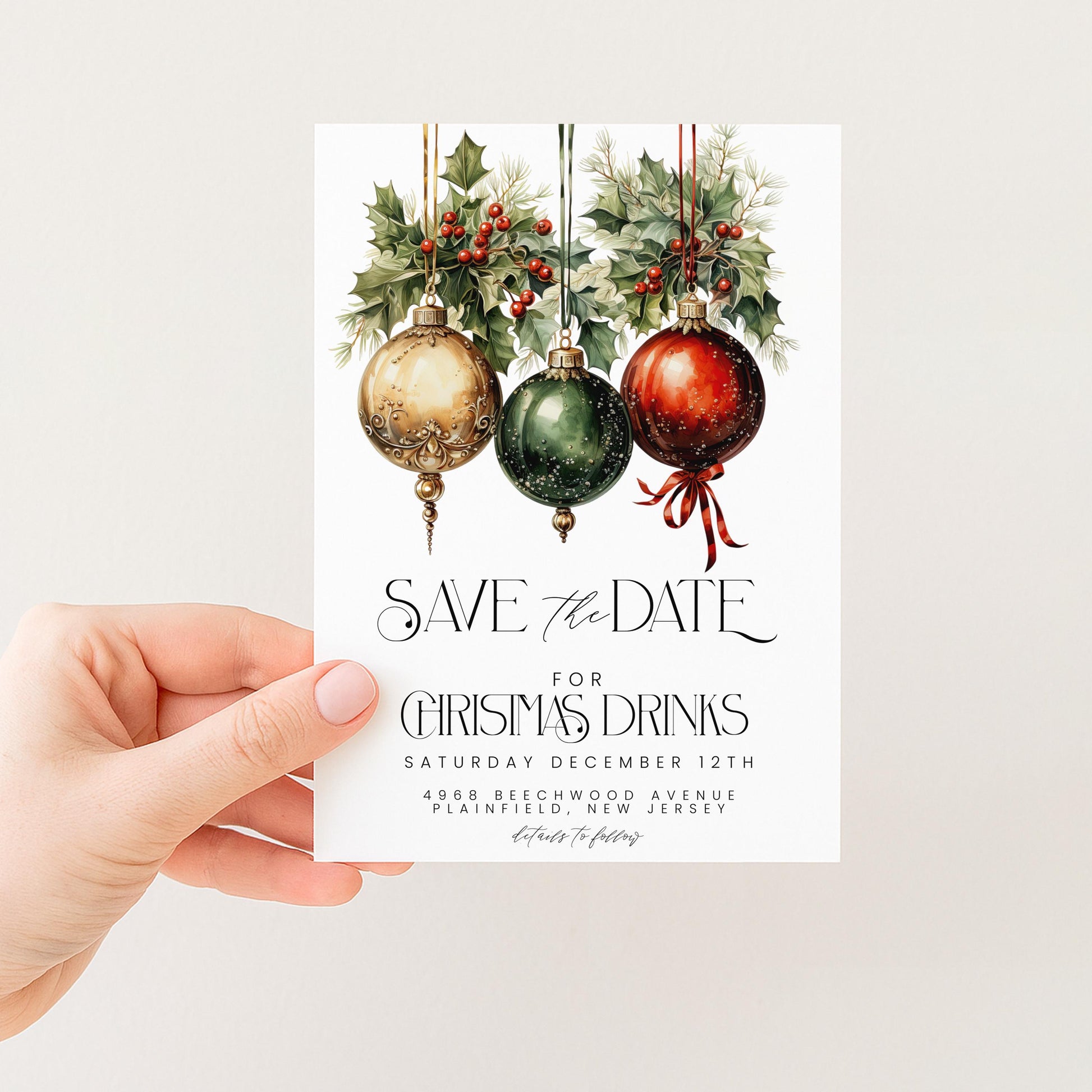 A hand holding a white card with a festive Christmas-themed design featuring three ornaments hanging from a branch with holly and berries.