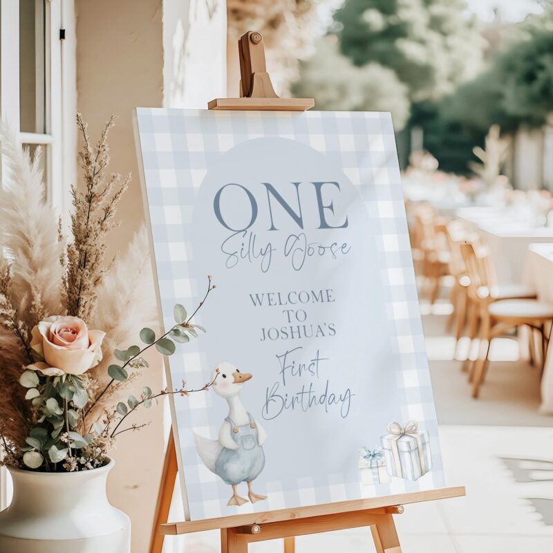 Editable blue gingham birthday welcome sign with goose in overalls and gift boxes, styled on an easel with eucalyptus greenery.