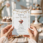 Baby-Q Save the Date invitation held with cupcakes and flowers in background
